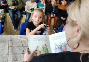 Członkowie Szkolnego Koła UNICEF siedzą i słuchają jak czyta pani.