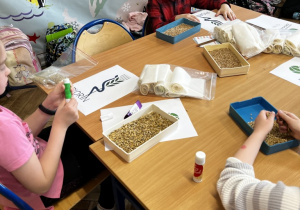 Uczniowie wykonują prace plastyczne wykorzystując nasiona.