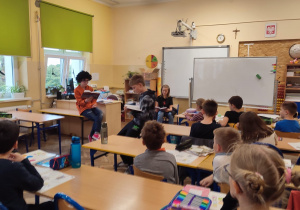 Uczniowie klas VI czytają książki uczniom klas młodszych.