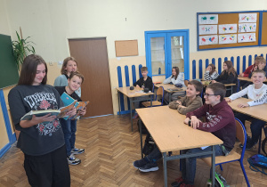 Uczniowie klas VI czytają książki uczniom klas młodszych.