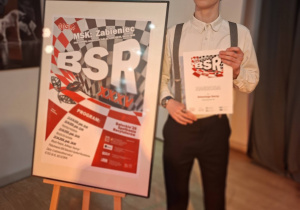 Antek Sarna na tle banera reklamujacego konkurs