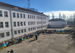 Widok na dziedziniec szkoły, uczniowie z flagami Ukrainy.